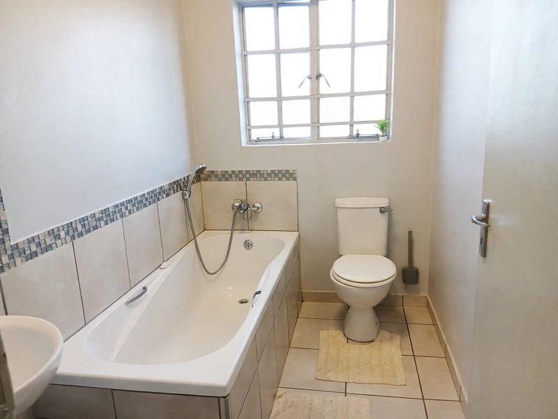 A functional bathroom featuring a bathtub with shower attachment, a toilet, and a basin, finished with neutral wall and floor tiles.