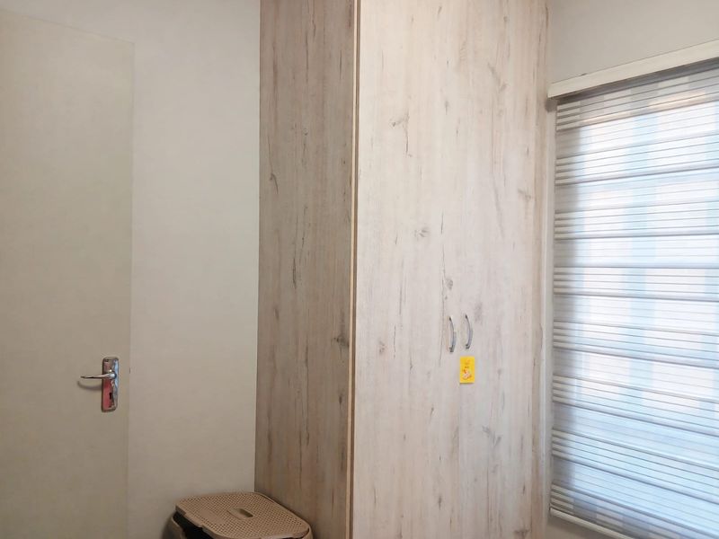 A clean bedroom interior featuring a modern light wood-grain built-in wardrobe and fitted roller blinds on the window.