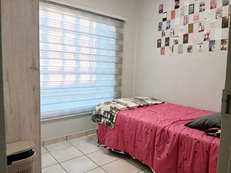 A functional bedroom featuring tiled flooring, a built-in cupboard, and modern zebra blinds, providing a clean and practical living space.