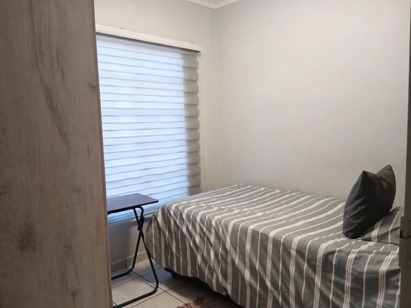 A compact bedroom featuring neutral wall finishes, tiled flooring, a built-in wardrobe, and modern roller blinds for privacy.