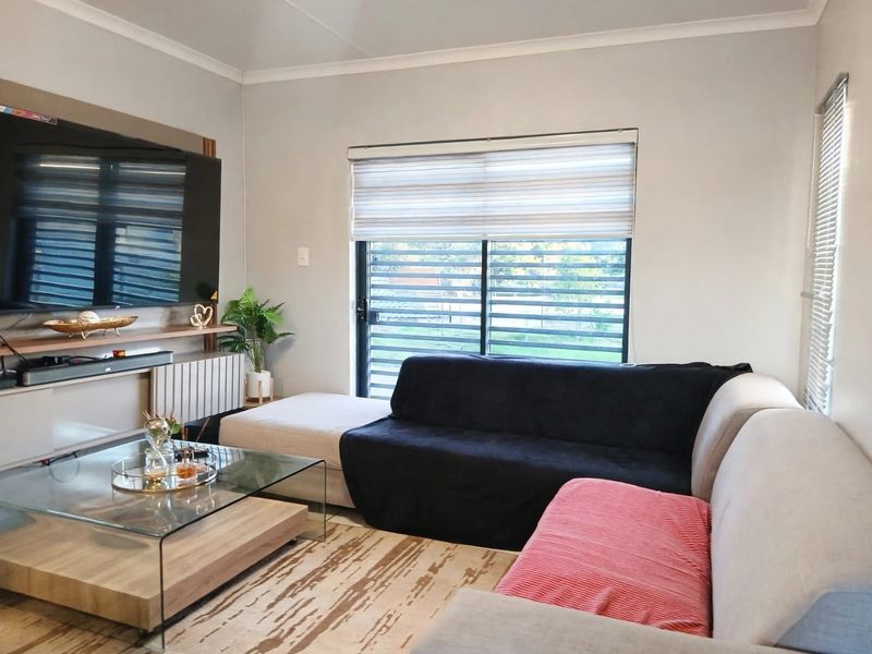 A well-maintained living room featuring a built-in media console, modern roller blinds, and large sliding windows that provide natural light.