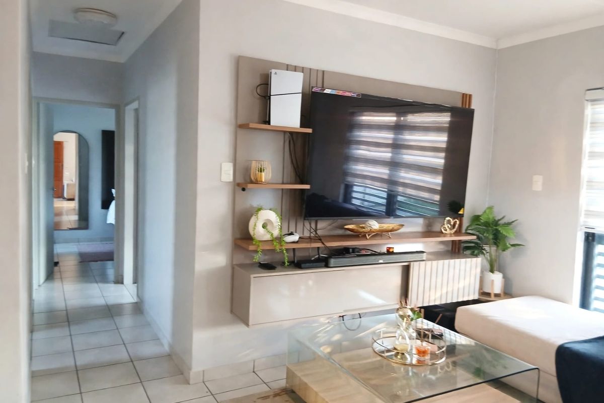 A well-maintained living room featuring a modern built-in media unit, neutral wall tones, and tiled flooring with access to a hallway.