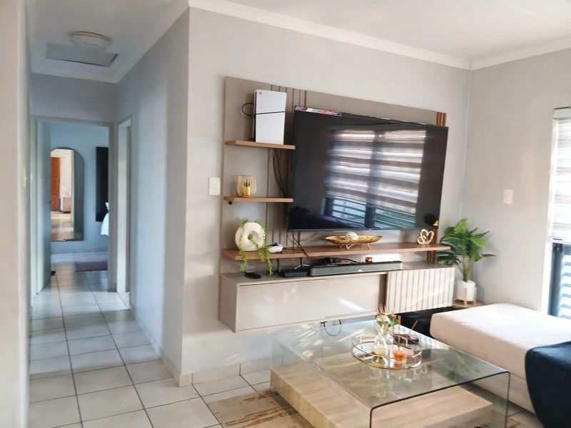 A well-maintained living room featuring a modern built-in media unit, neutral wall tones, and tiled flooring with access to a hallway.