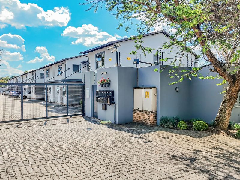 Front entrance view of the townhouse complex featuring a secure gated access point, paved driveway, and perimeter wall with electric fencing.