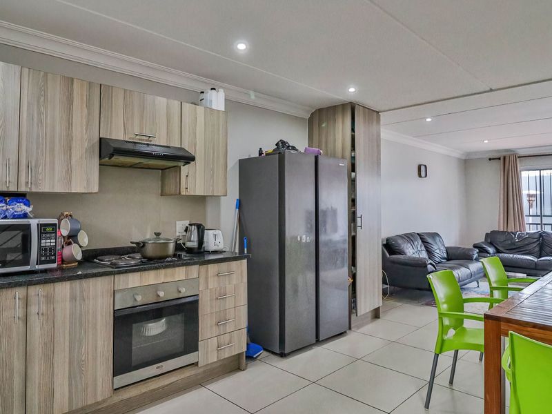 Open-plan living area featuring a modern kitchen with wood-grain cabinetry, built-in oven, and hob, flowing into a spacious dining and lounge area with tiled floors.