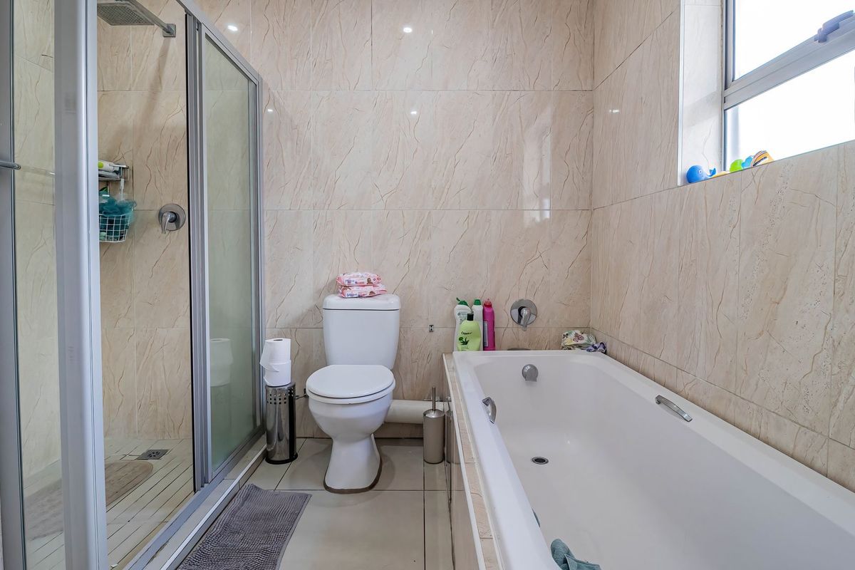 A functional bathroom featuring a glass-enclosed shower, a built-in bathtub, and full-height wall tiling.