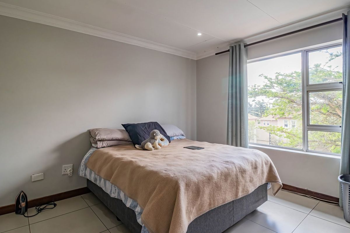 A well-lit bedroom featuring neutral wall tones, tiled flooring, and a large window providing natural light and an exterior view.