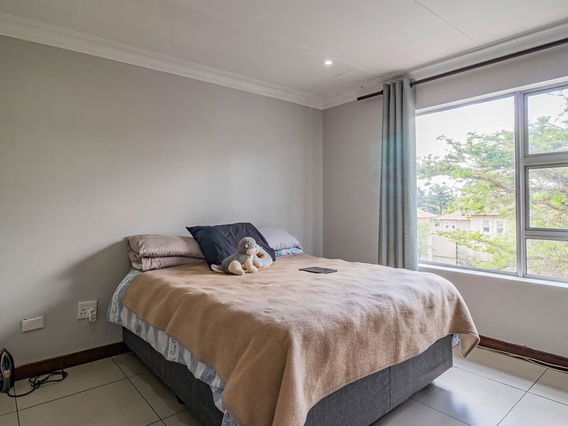 A well-lit bedroom featuring neutral wall tones, tiled flooring, and a large window providing natural light and an exterior view.