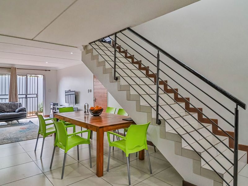 Open-plan living and dining area featuring tiled flooring, recessed lighting, and a staircase with a metal balustrade leading to the upper level.