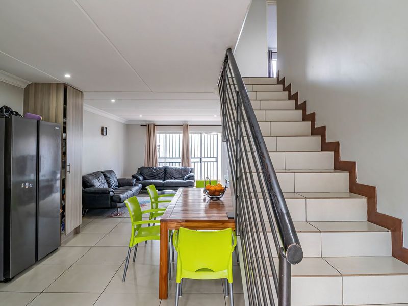 Open-plan living and dining area featuring tiled flooring, recessed lighting, and a staircase with a metal railing leading to the upper level.
