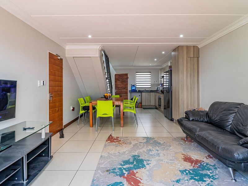 An open-plan living, dining, and kitchen area featuring tiled floors, recessed lighting, and a staircase, creating a functional and cohesive living space.