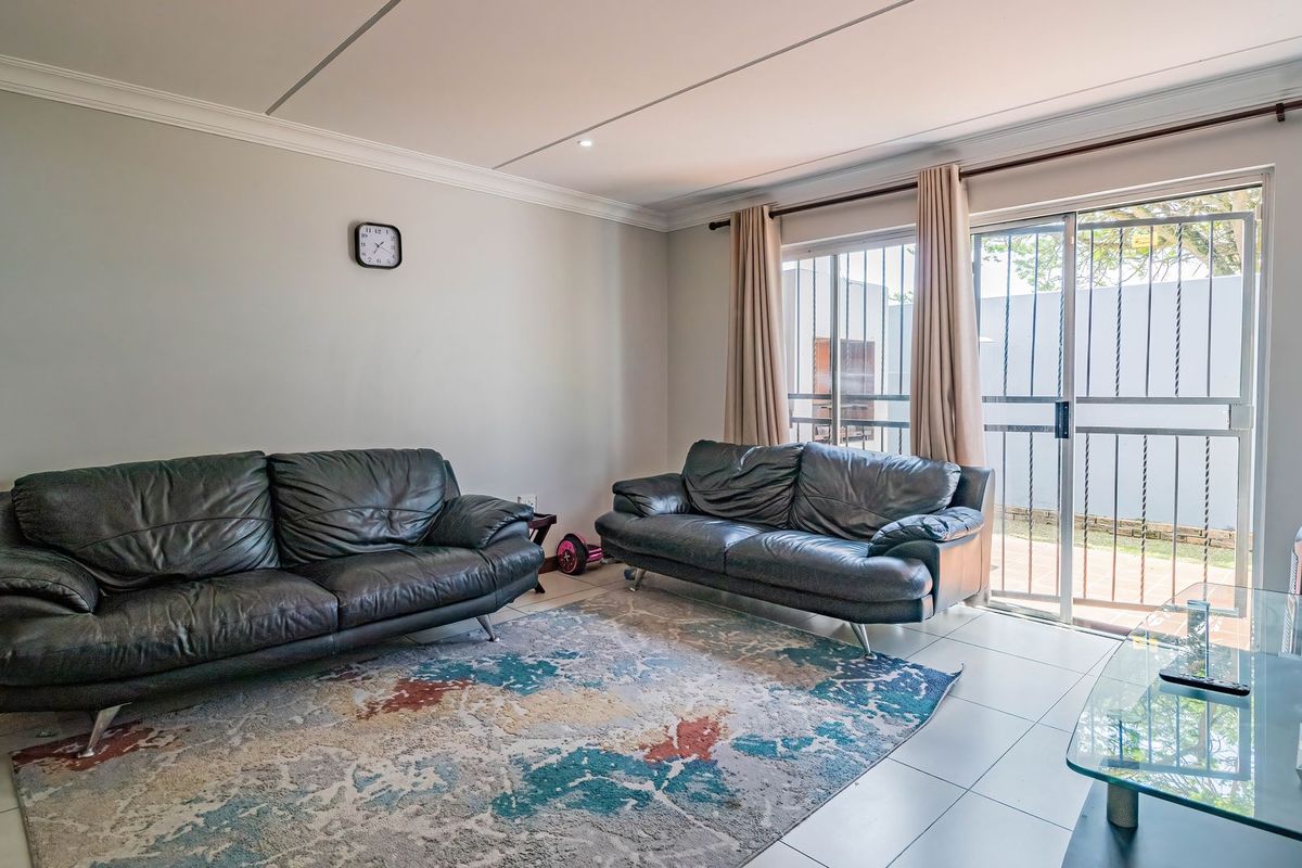A bright living room featuring tiled flooring, recessed lighting, and a sliding glass door with security gate providing access to the outdoor area.