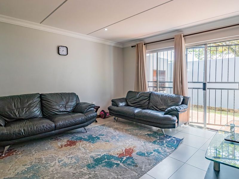 A bright living room featuring tiled flooring, recessed lighting, and a sliding glass door with security gate providing access to the outdoor area.