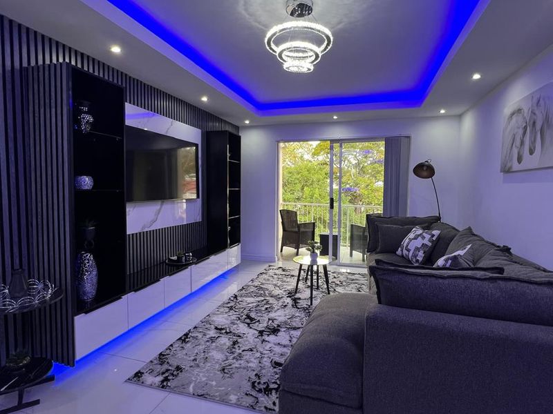 Modern living room featuring a custom built-in media wall with slatted paneling, recessed blue LED ceiling lighting, and polished porcelain floor tiles.