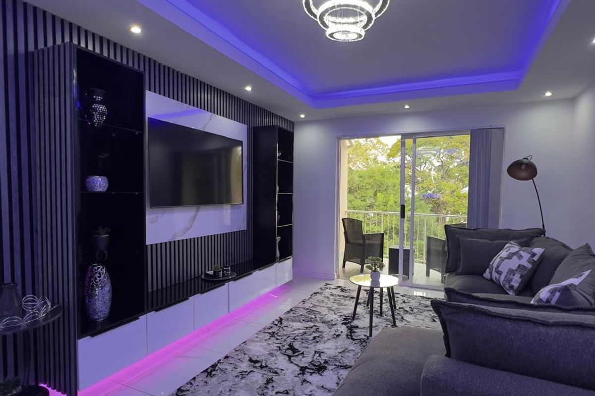 Modern living room featuring a custom built-in media wall with slatted paneling, integrated LED lighting, cove ceiling, and polished porcelain floor tiles.
