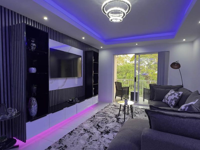 Modern living room featuring a custom built-in media wall with slatted paneling, integrated LED lighting, cove ceiling, and polished porcelain floor tiles.