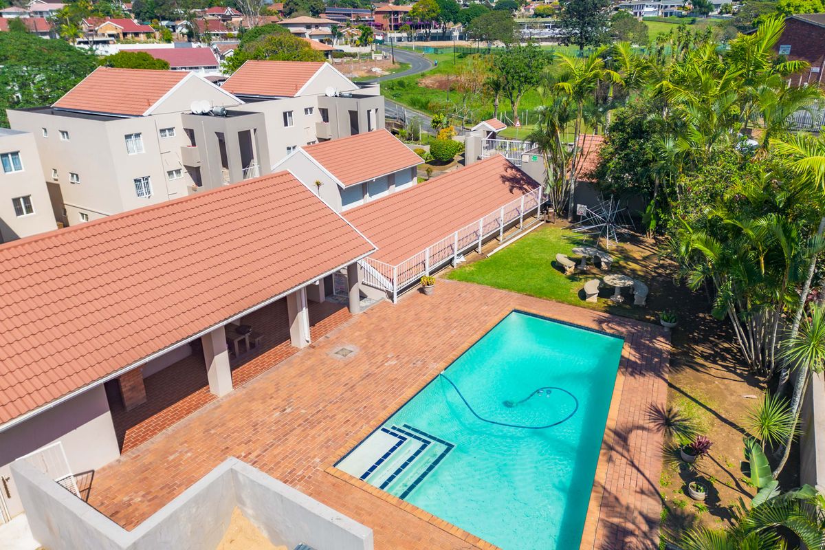 Aerial view of the townhouse complex featuring a communal swimming pool, brick-paved patio area, covered veranda, and well-maintained garden surroundings.