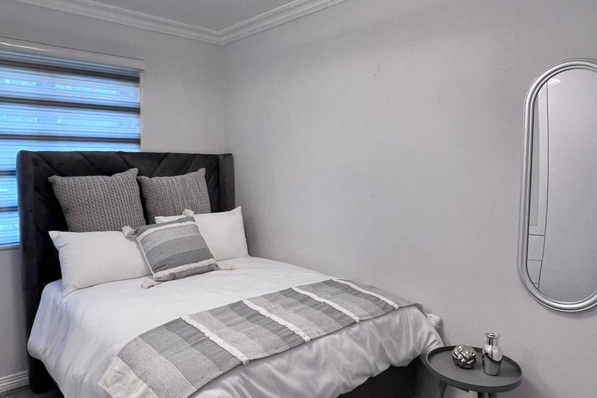 A well-maintained bedroom featuring modern laminate flooring, crown molding, and a contemporary ceiling light fixture, creating a clean and neutral living space.