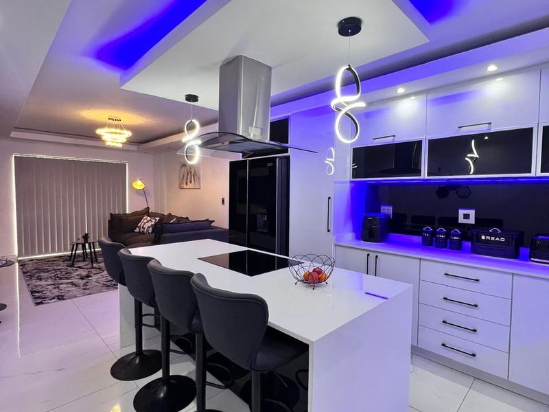 Modern open-plan kitchen and living area featuring a central island with hob, sleek cabinetry, and contemporary recessed LED lighting.