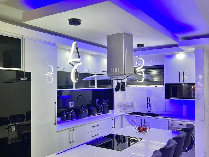 Modern kitchen featuring a central island with built-in hob, sleek cabinetry, stone countertops, and ambient LED drop ceiling lighting.