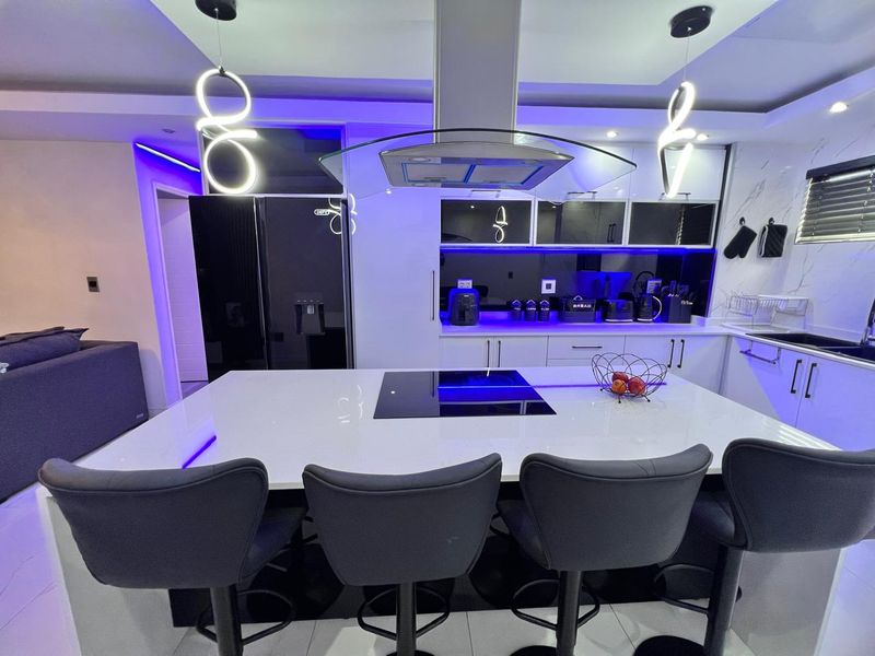 Modern kitchen featuring a large central island with a built-in hob, sleek cabinetry, quartz countertops, and integrated ambient LED lighting.