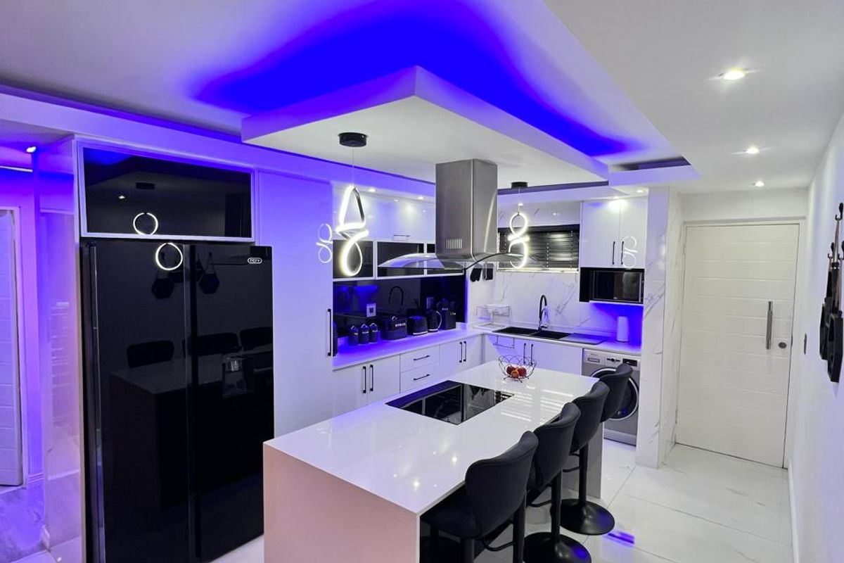 Modern kitchen featuring a central island with integrated hob, sleek cabinetry, marble-look flooring, and sophisticated LED accent lighting throughout.