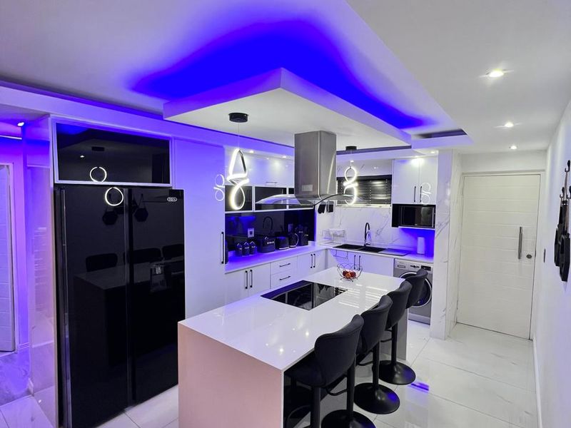 Modern kitchen featuring a central island with integrated hob, sleek cabinetry, marble-look flooring, and sophisticated LED accent lighting throughout.