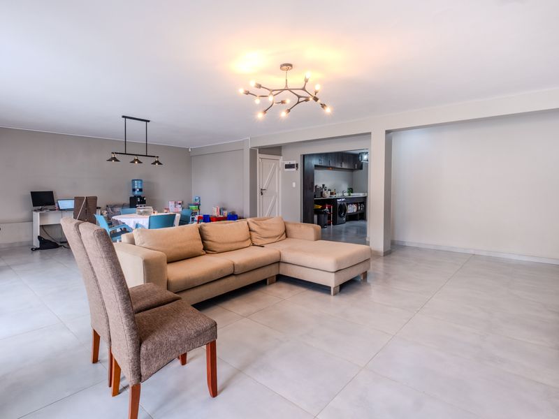 Spacious open-plan living area featuring large format floor tiles, modern lighting, and an integrated kitchen space, offering a versatile and bright layout.