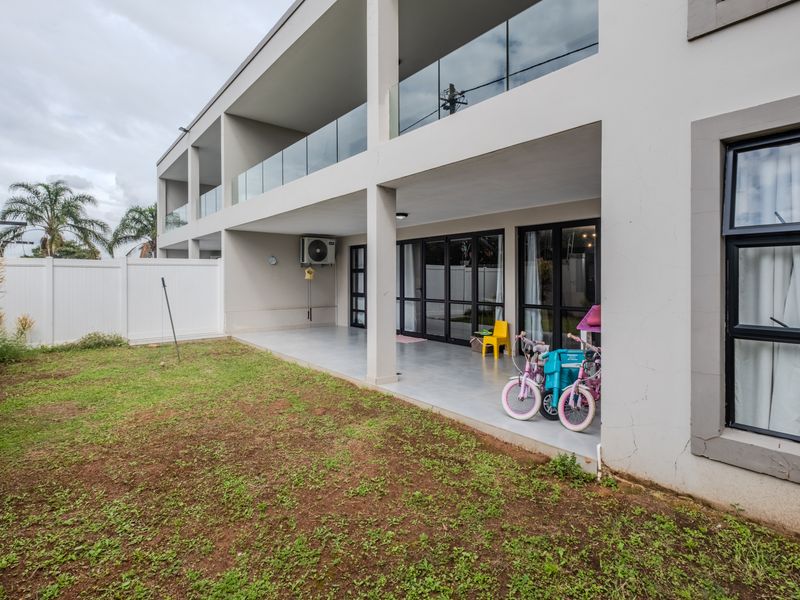 Rear view of a modern apartment building featuring a covered patio, glass balustrades, and access to a private garden area.