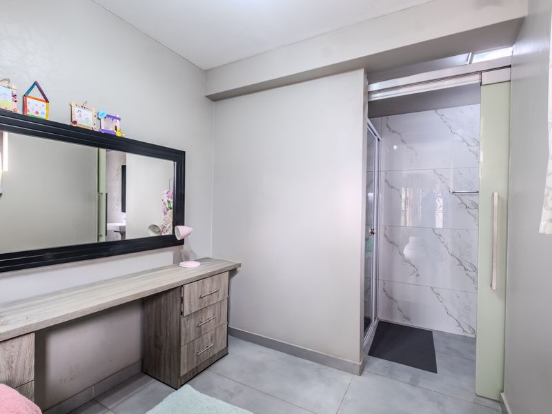 Bedroom featuring a built-in vanity unit and an en-suite bathroom with a modern shower enclosure and marble-look wall tiling.