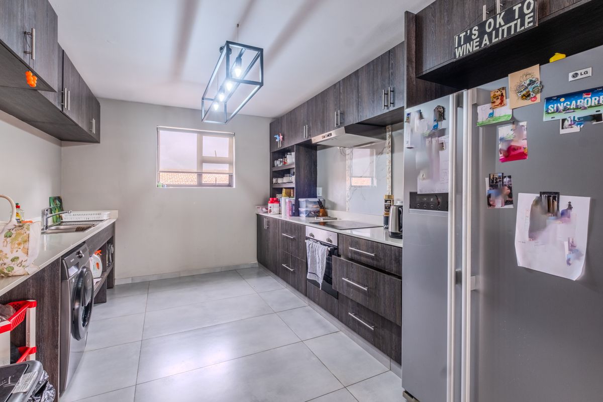 Modern kitchen featuring dark wood cabinetry, stone countertops, integrated appliances, and tiled flooring with a functional layout.