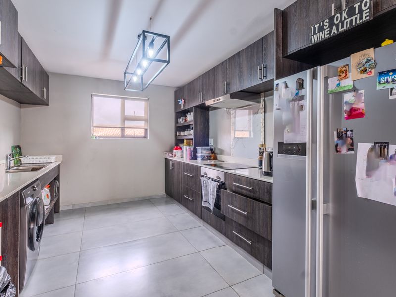 Modern kitchen featuring dark wood cabinetry, stone countertops, integrated appliances, and tiled flooring with a functional layout.