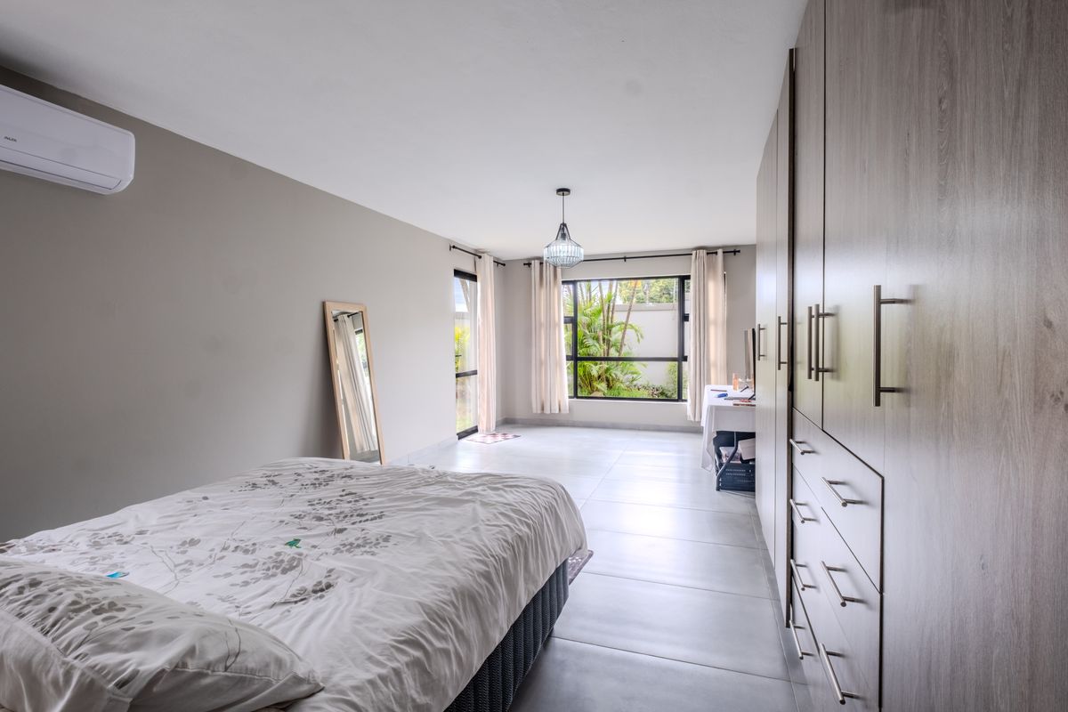 Spacious bedroom featuring modern built-in cupboards, tiled flooring, and an air conditioning unit, with large windows providing natural light and garden views.