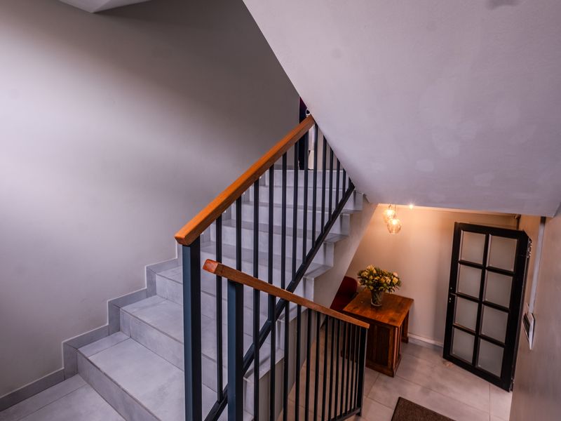 A modern interior hallway featuring a tiled staircase with a metal balustrade, wooden handrail, and a glass-paneled door leading to an adjacent space.