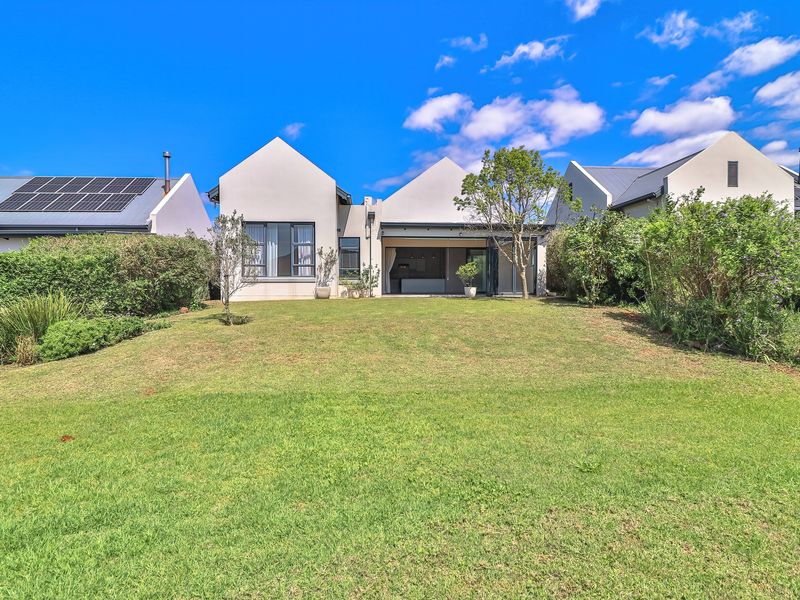 A well-maintained rear exterior view of the house featuring a spacious lawn, mature garden hedging, and modern architectural roof lines.