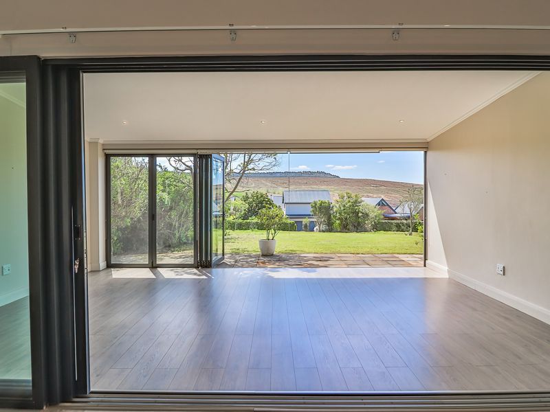 Spacious living area featuring modern laminate flooring and large aluminium stacker doors that open onto a paved patio and garden.