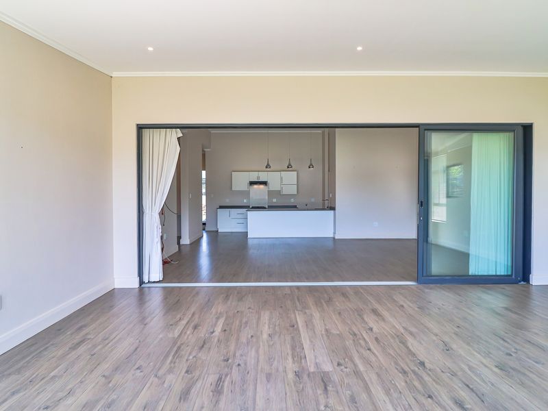 Spacious open-plan living area featuring modern laminate flooring, recessed lighting, and large sliding glass doors leading to an integrated kitchen with contemporary cabinetry.