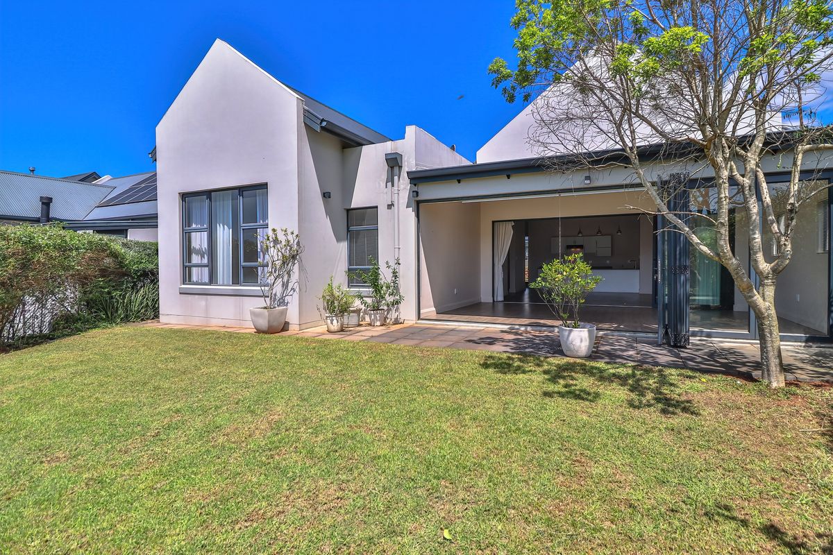 Rear view of the property featuring a paved patio, landscaped garden, and large bi-fold doors providing seamless indoor-outdoor flow.