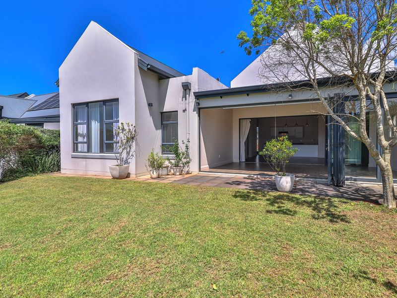 Rear view of the property featuring a paved patio, landscaped garden, and large bi-fold doors providing seamless indoor-outdoor flow.