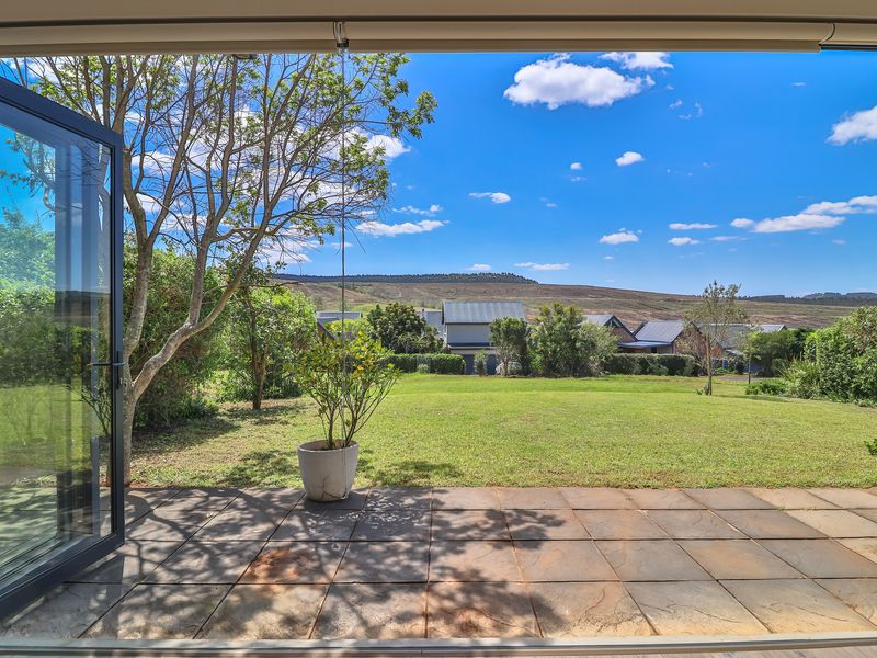 A covered patio area featuring tiled flooring and bi-fold doors, opening onto a spacious garden with scenic mountain views.