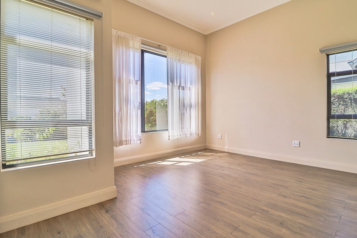 A bright and spacious empty bedroom featuring modern laminate flooring, neutral walls, and large windows with fitted blinds, offering a clean and versatile living space.