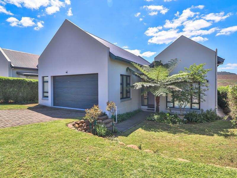 A well-maintained modern house exterior featuring a paved driveway, integrated garage, and landscaped front garden under a clear blue sky.