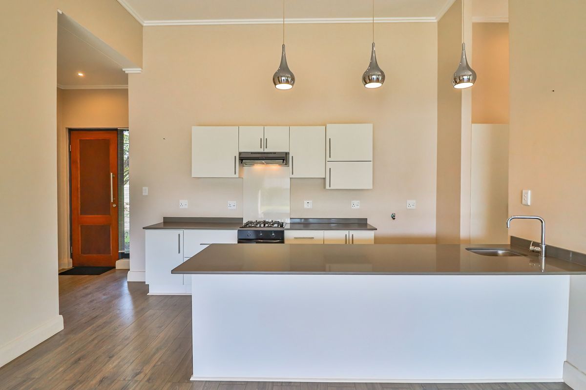 Modern kitchen featuring clean white cabinetry, stone countertops, a central island with sink, and integrated gas hob with extractor fan.