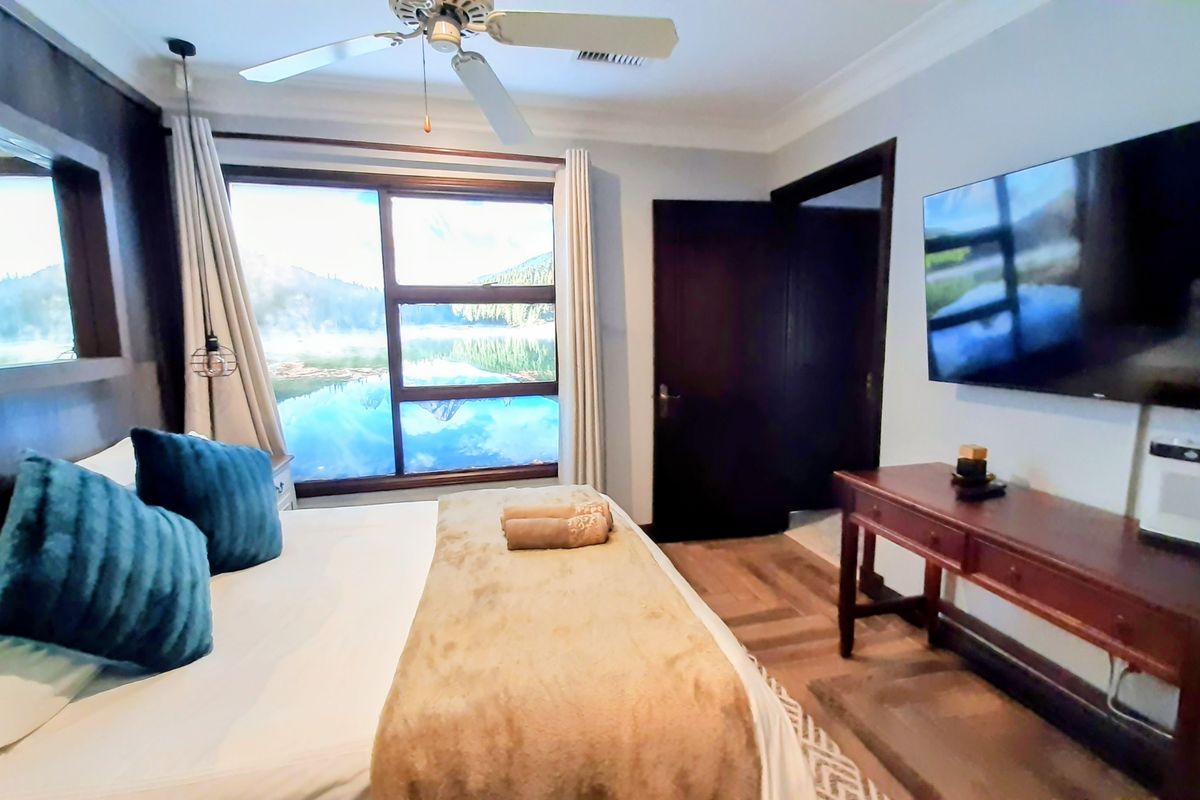 A well-maintained bedroom featuring hardwood flooring, crown molding, a ceiling fan, and a large window providing natural light.