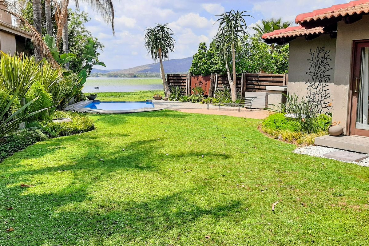 A well-maintained rear garden featuring a swimming pool, wooden decking, and scenic lake views, adjacent to a home with a tiled roof.