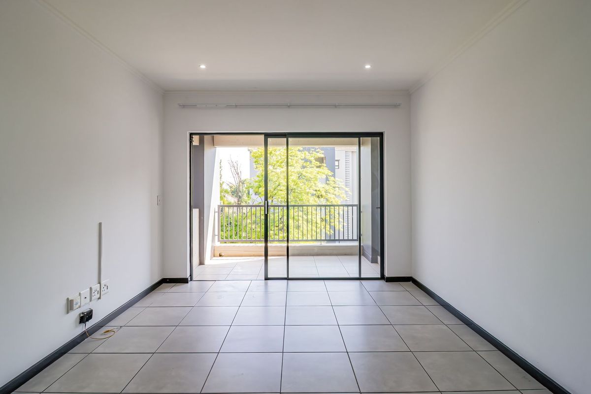 A bright, empty living room featuring neutral tiled flooring, recessed lighting, and a large sliding glass door leading to an outdoor balcony.