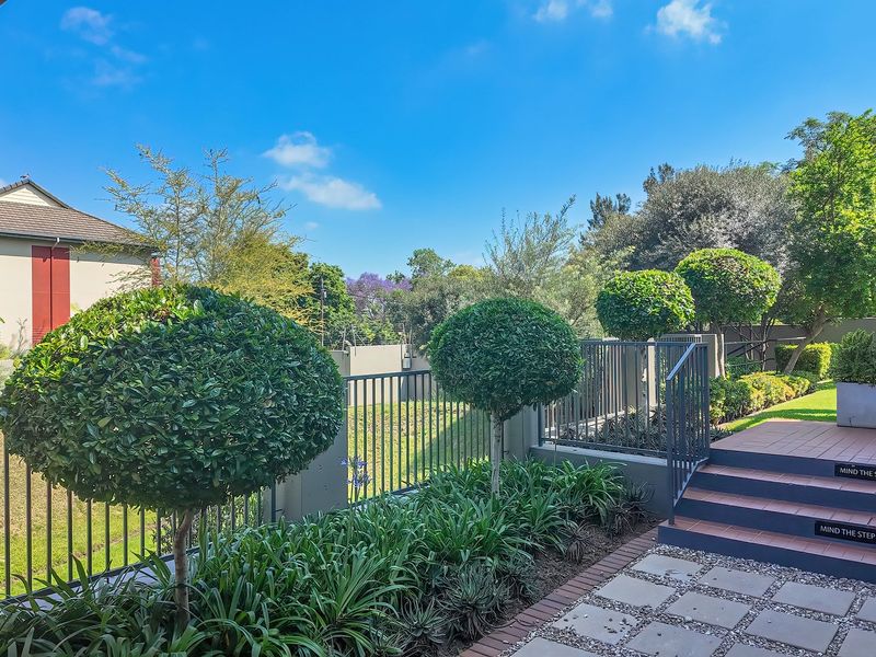 A well-maintained outdoor patio area featuring a tiled staircase with metal balustrades, leading to a landscaped garden with manicured shrubs.