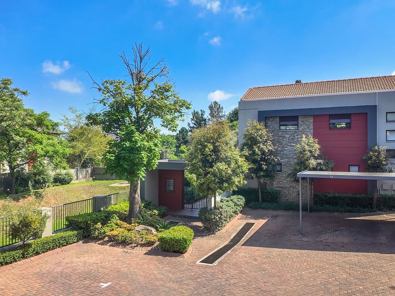 Front exterior view of the apartment complex featuring a brick paved driveway, covered carport, and landscaped garden area.