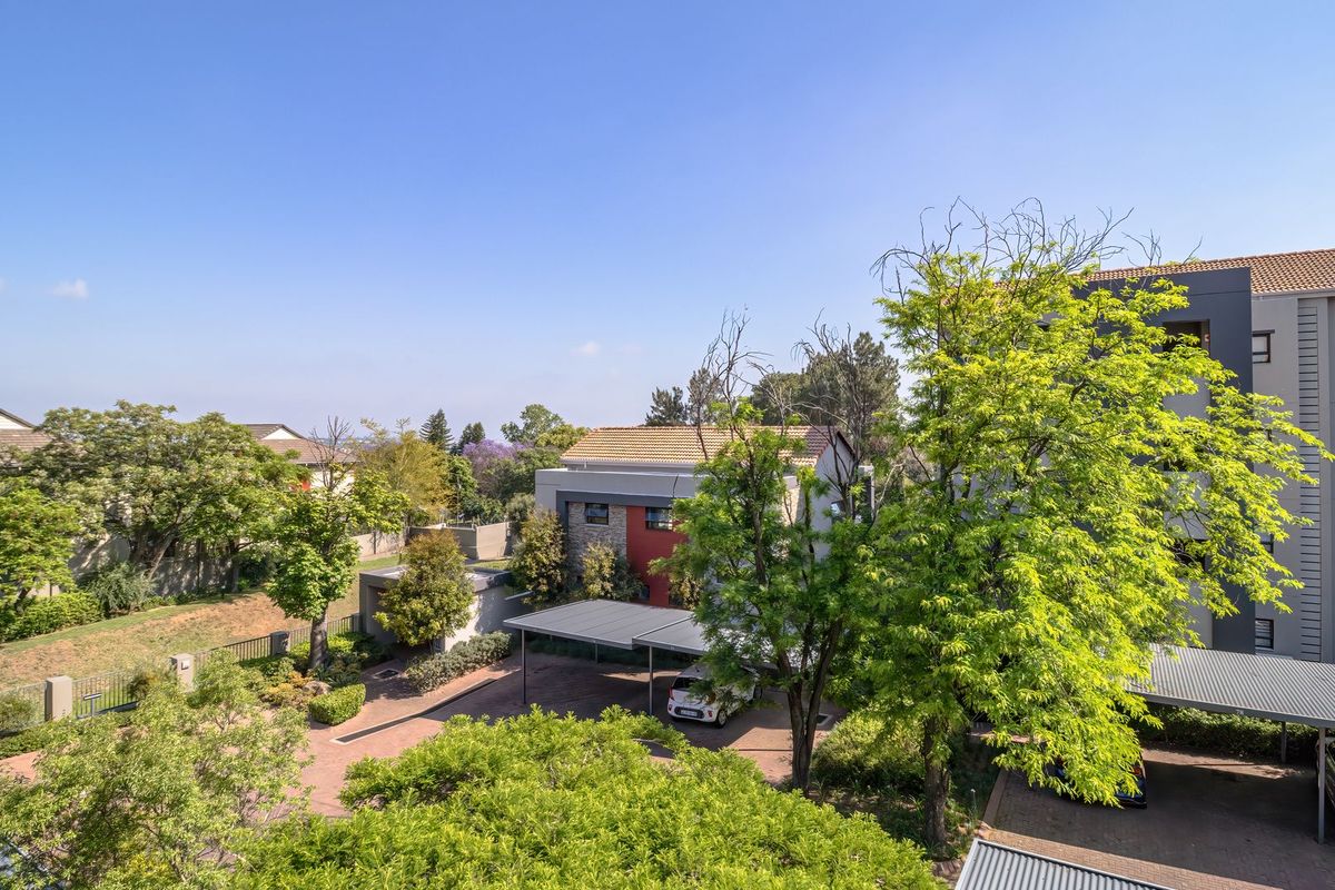 An elevated view of the apartment complex grounds, featuring paved driveways, covered parking bays, and established garden areas.