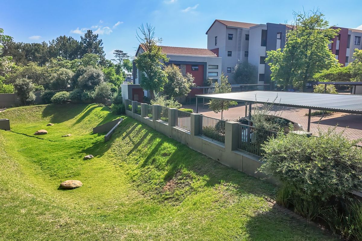 A well-maintained exterior view of the apartment complex featuring a landscaped garden, secure perimeter fencing, and covered carport parking.